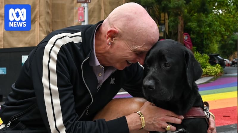 Scott Dixon-Smith smiling beside his golden retriever guide dog Pretzel wearing service harness