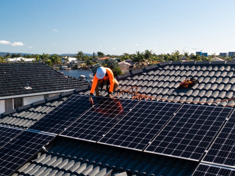 Solar panels on Australian rooftop reflecting sunlight with blue sky background and battery storage unit
