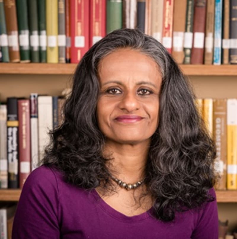 Professor in university library surrounded by diverse international literature and books on postcolonial studies and global democracy