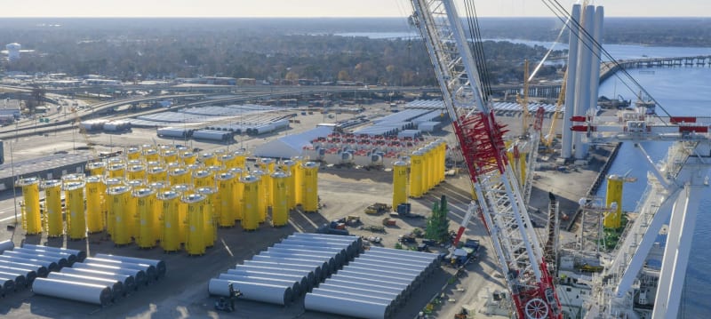 Offshore wind turbine components and support ships at marine terminal staging area for construction