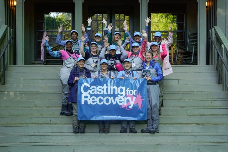 Breast cancer survivors learning fly fishing techniques together at peaceful mountain stream retreat