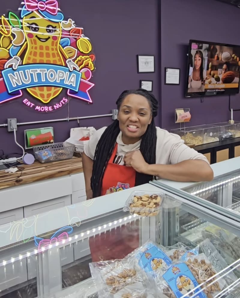 Shantell Reid stands inside Nuttopia candy store surrounded by colorful gourmet sweets and nuts