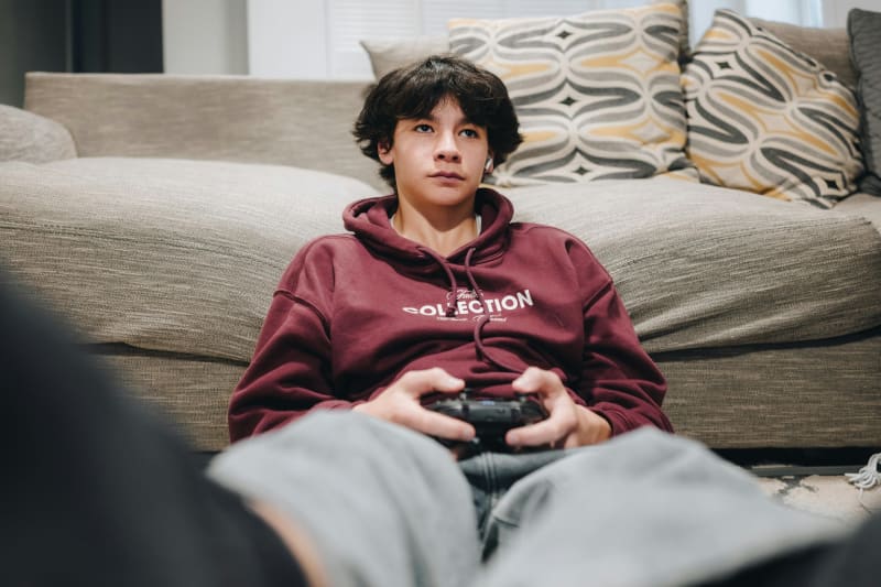 Young teenager playing video games on computer in comfortable home setting with family nearby