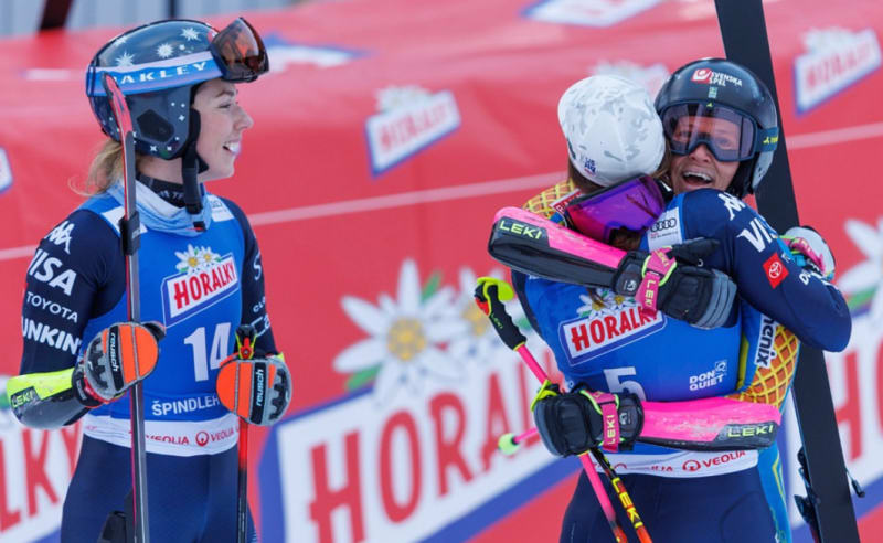 Three female skiers standing on World Cup podium holding flowers and celebrating their giant slalom results