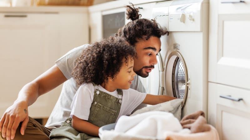 Father and young son sitting together doing laundry, showing positive male mentorship and connection