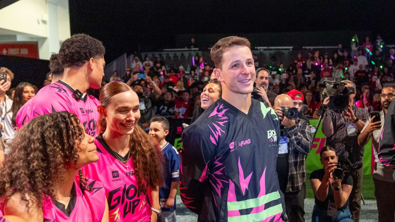 Brock Purdy coaching young female flag football players in glowing uniforms at indoor venue