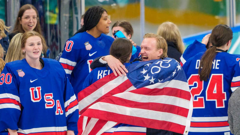 Coach John Wroblewski wiping tears while Team USA women's hockey players celebrate Olympic gold medal victory