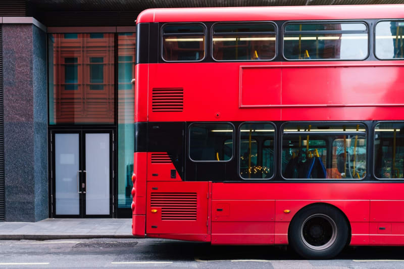 Bus driver Mark Hehir standing beside London double-decker bus in uniform smiling