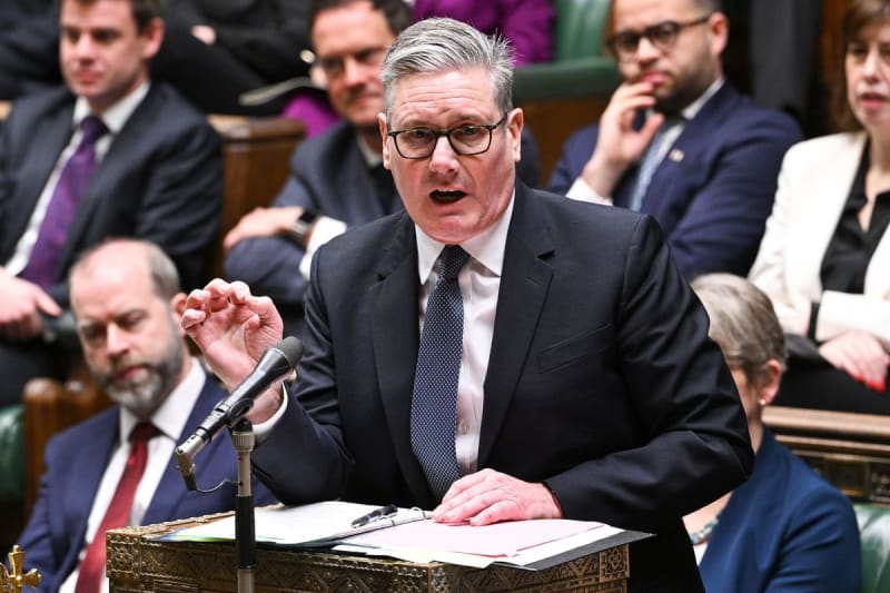 Parent holding newborn baby while working on laptop at home office desk