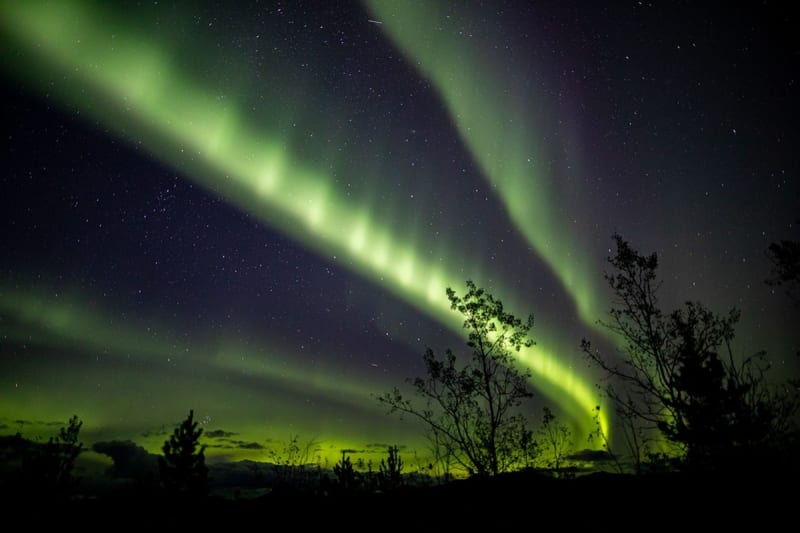 Green aurora arc stretching across dark night sky above northwestern Canada landscape