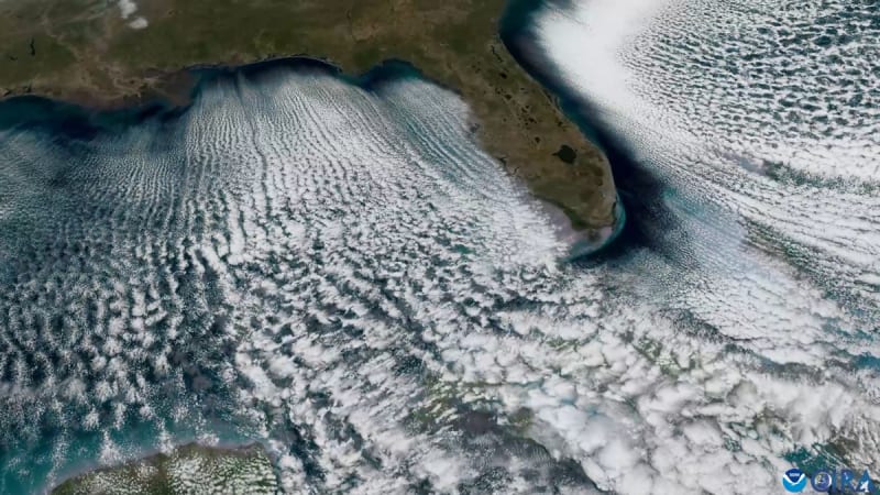 Satellite view showing parallel white cloud lines streaming over blue ocean waters near Florida coast