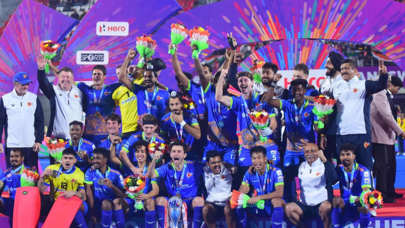 Hockey players celebrating championship victory on home stadium field with crowd cheering