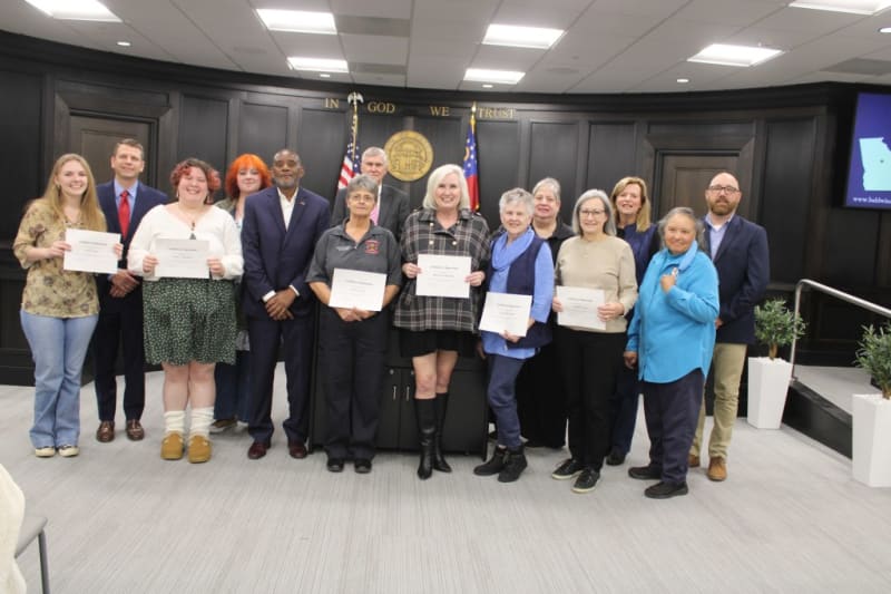 Volunteers and county commissioners pose together holding certificates of appreciation for Christmas gift wrapping service