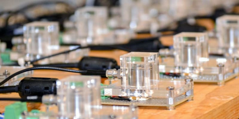 MIT engineers examining battery monitoring equipment with visual sound wave displays showing acoustic emissions from lithium-ion batteries