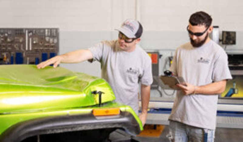 Student working on laptop with automotive textbooks and scholarship application materials nearby