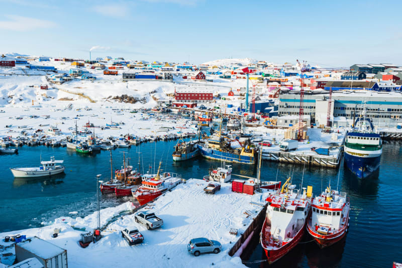 Scenic view of Ilulissat port in Greenland showing colorful buildings against Arctic waters and icebergs