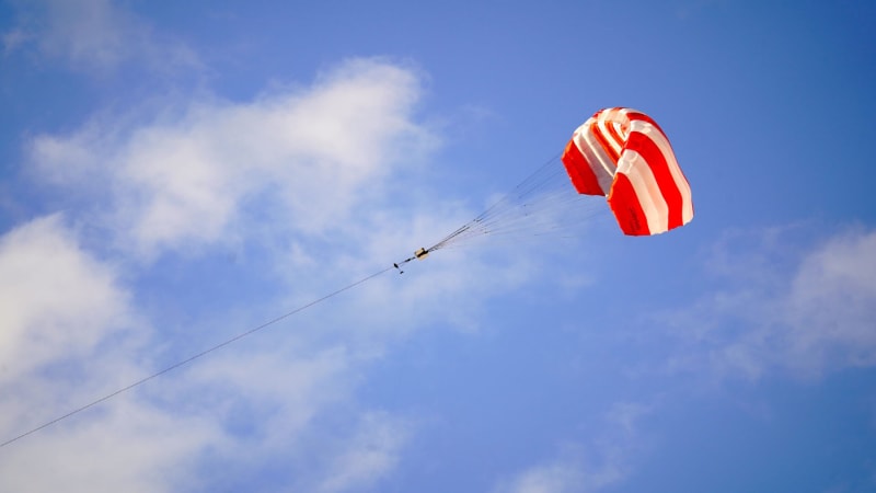 Large kite flying high in blue sky connected by tether to ground-based shipping container power generator