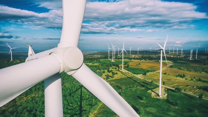 Advanced autonomous drone inspecting tall white wind turbine blade against blue sky