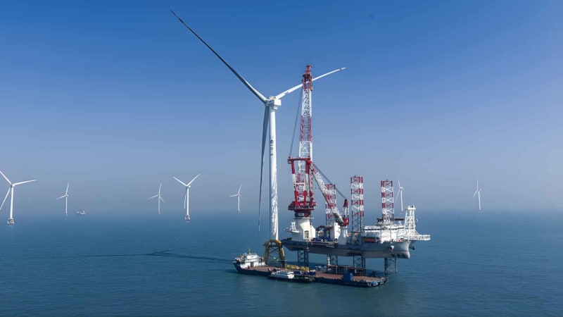 ** Massive offshore wind turbine with giant rotor blades spinning above ocean waves near Hainan coast