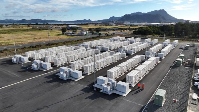 Large battery energy storage facility with solar panels in background under clear sky