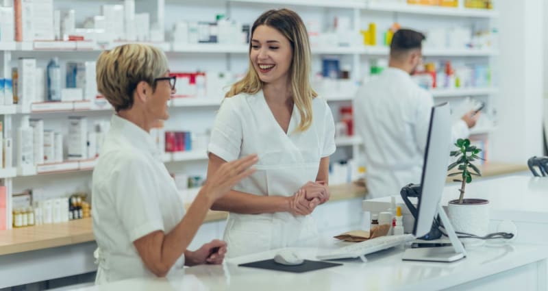 Two coworkers enjoying coffee and conversation during workplace break in bright Swedish pharmacy