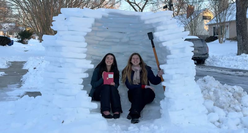 Two teenage girls standing inside homemade igloo with ice chairs and table in Maryland neighborhood