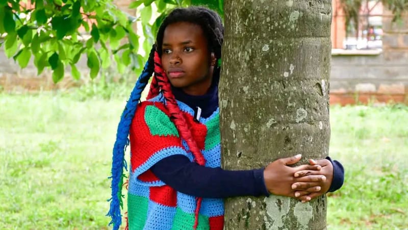 Young Kenyan woman in green outfit embracing large tree trunk during world record attempt