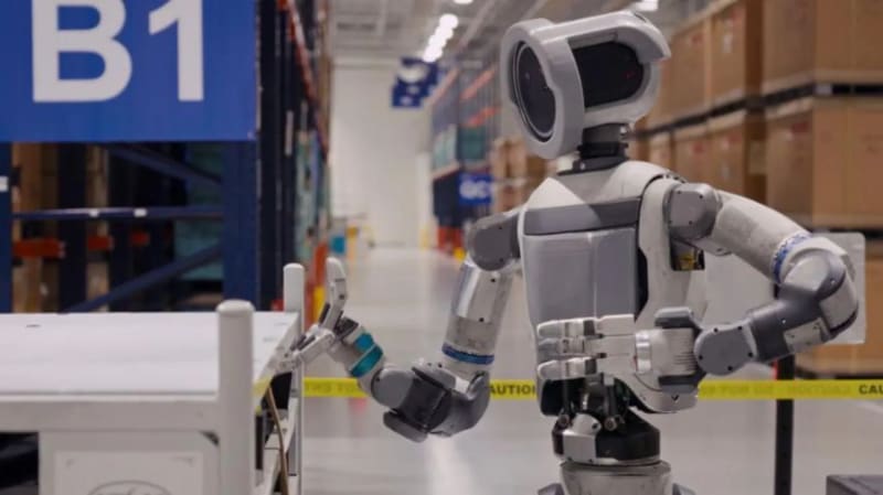 Hyundai's Atlas humanoid robot standing in modern factory setting alongside human workers in collaborative workspace