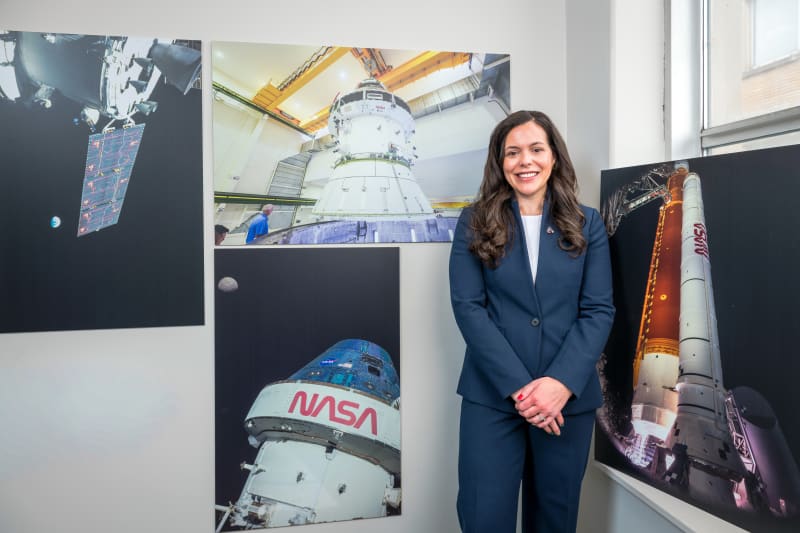 Katie Oriti in NASA polo shirt smiling at camera, standing in front of American flag