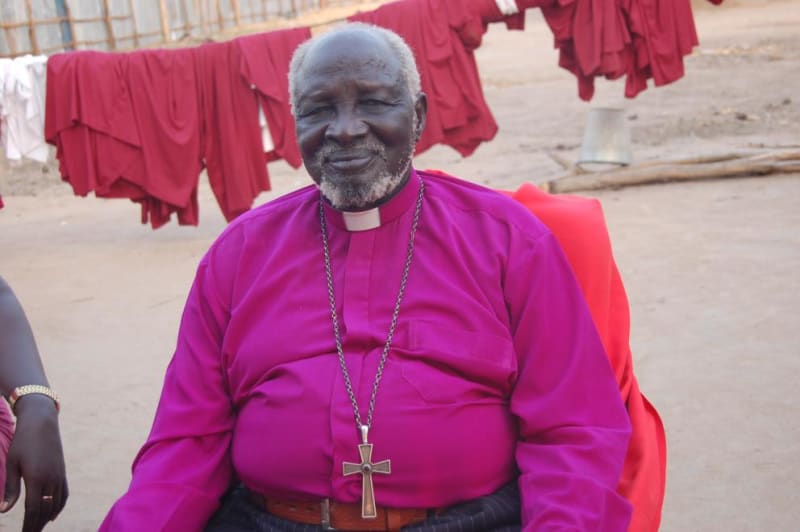 Elderly Bishop Nathaniel Garang in white Anglican vestments smiling warmly at camera