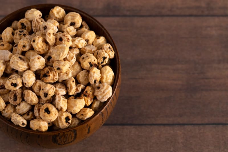 Close-up of small, wrinkled brown tiger nut tubers in a wooden bowl on kitchen counter