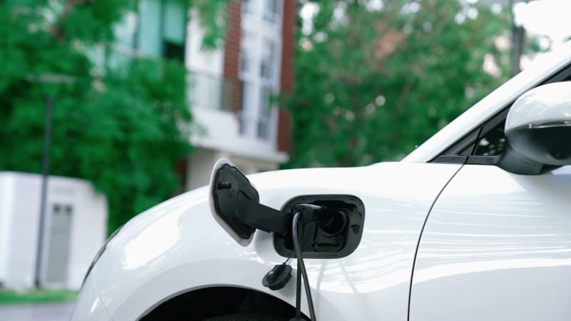Electric vehicle charging at modern public station with green landscaping and solar panels
