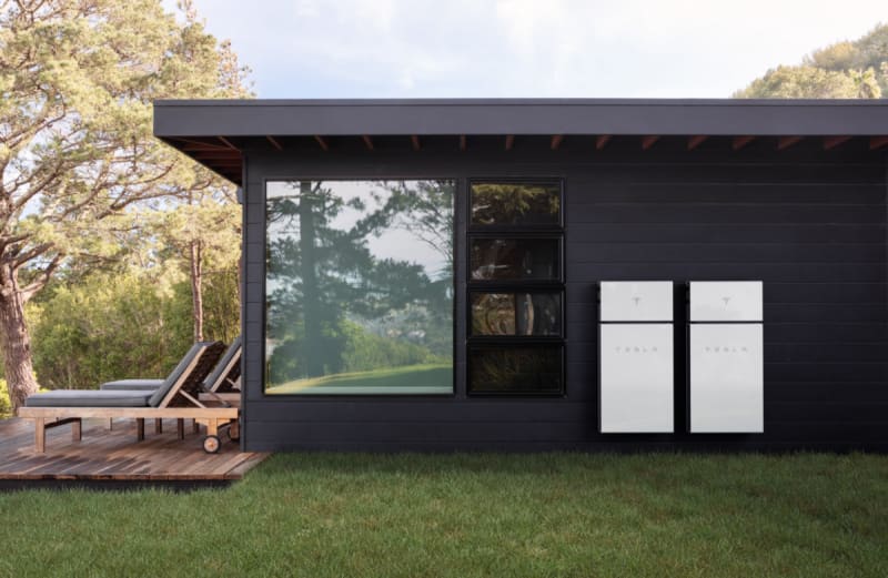 Home battery storage system mounted on residential wall with solar panels on roof