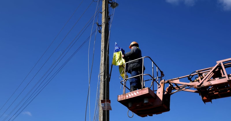 Electrical worker repairs damaged power line on tall metal pylon in rural Ukraine