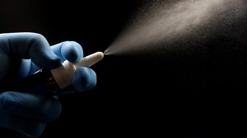 Scientist holding nasal spray vaccine in laboratory researching bird flu prevention methods