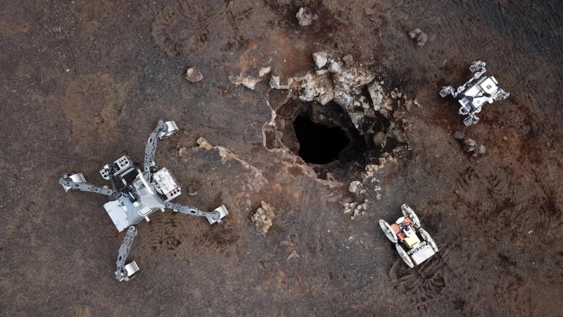 Three robots exploring dark volcanic cave entrance in Lanzarote Spain preparing for Moon missions