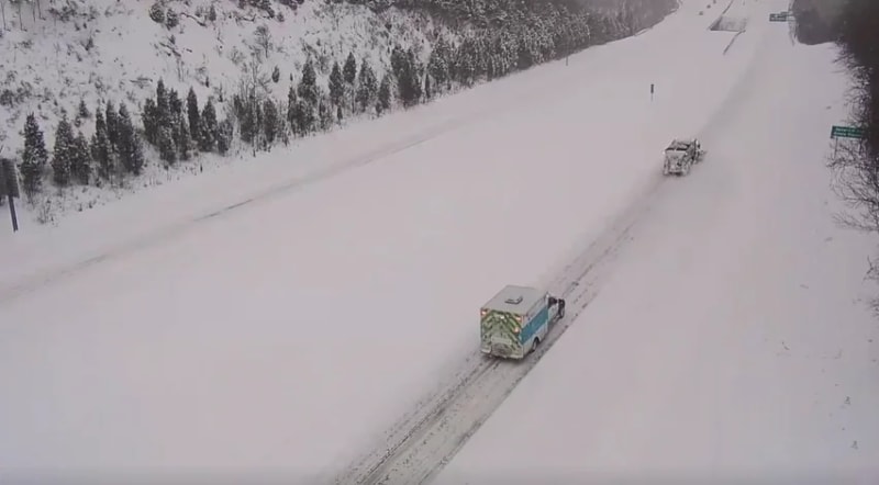 Snowplow truck clearing snowy road ahead of ambulance during winter storm in Cincinnati