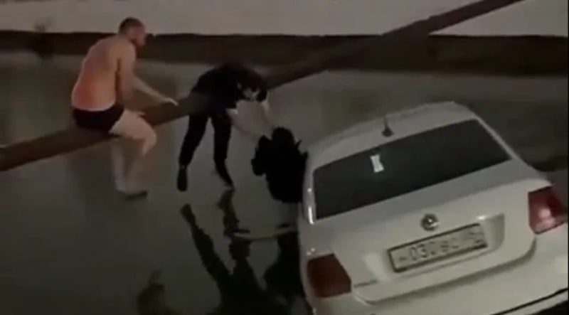Three men on metal pipe rescuing child from taxi submerged in Russian canal
