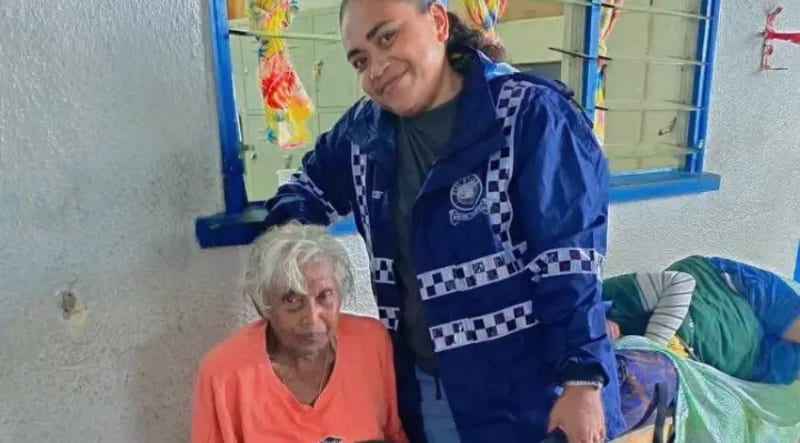 Police officer in uniform helping elderly woman during flooding in Fiji