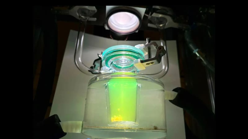 Hydrogen gas bubbles rising in beaker of water with conductive plastic nanoparticles under simulated sunlight