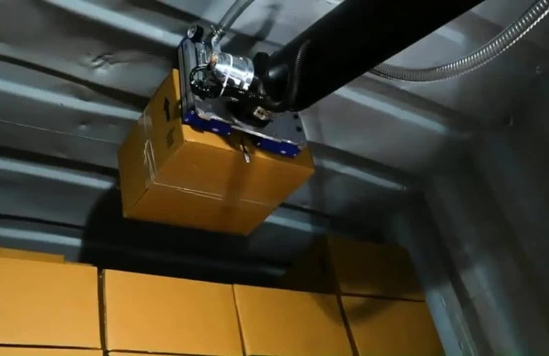 Advanced robotic arm with suction gripper system unloading packages from delivery truck in modern warehouse facility