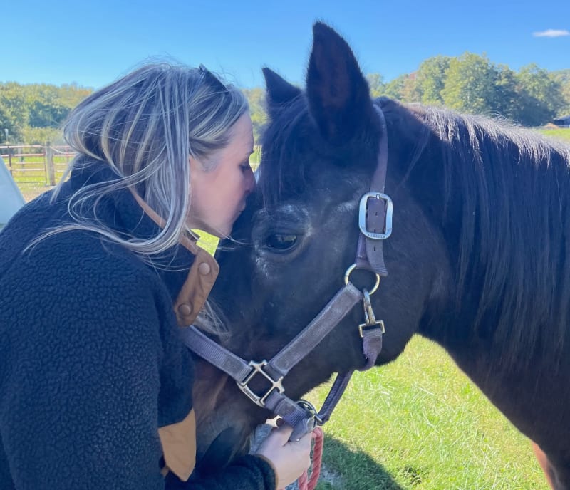 Elderly brown quarter horse Fancy standing beside lifelong caretaker Paige Blumer in Virginia stable