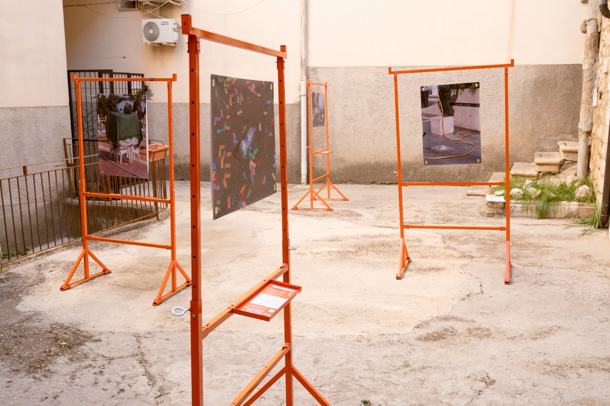 Four orange frames holding the prints, set up in the courtyard