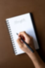 Someone writing in a book the word "Thoughts"
