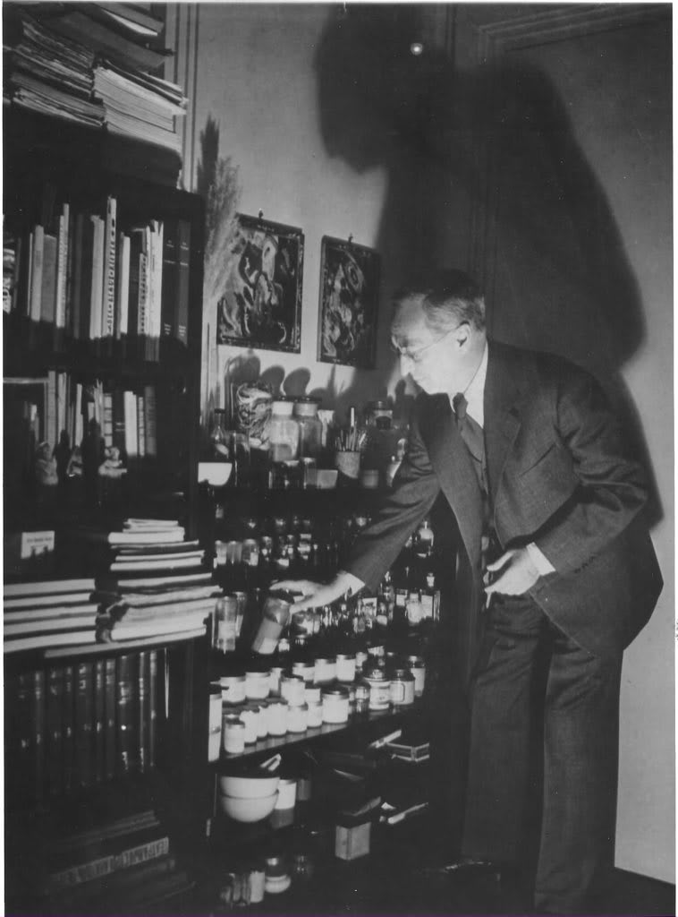 Vintage black and white photograph showing Wassily Kandinsky selecting pigments in his Paris atelier surrounded by books and 