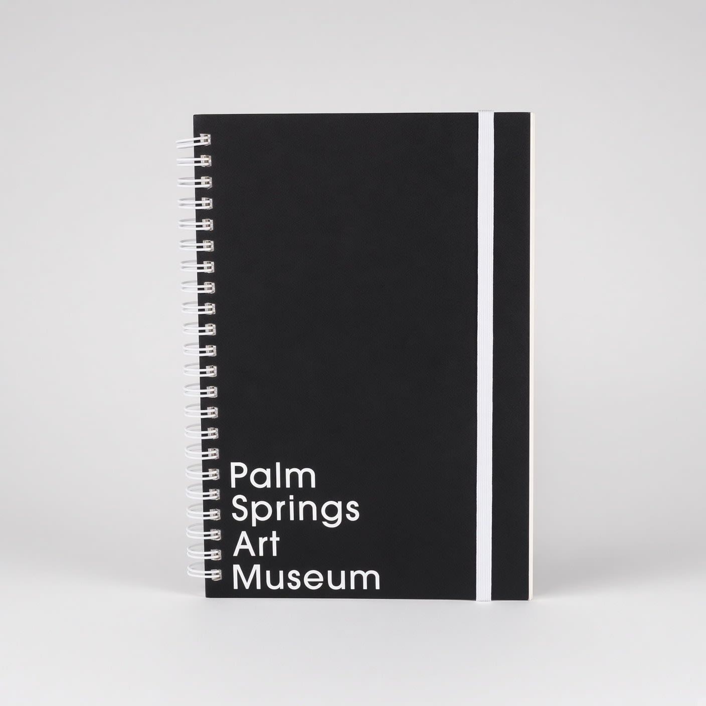 The black wire-bound notebook seen straight on, with its white elastic band.