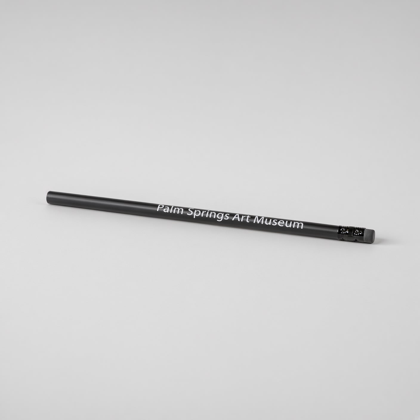 Black pencil lying on its side, with a black eraser and Palm Springs Art Museum in white along the barrel.