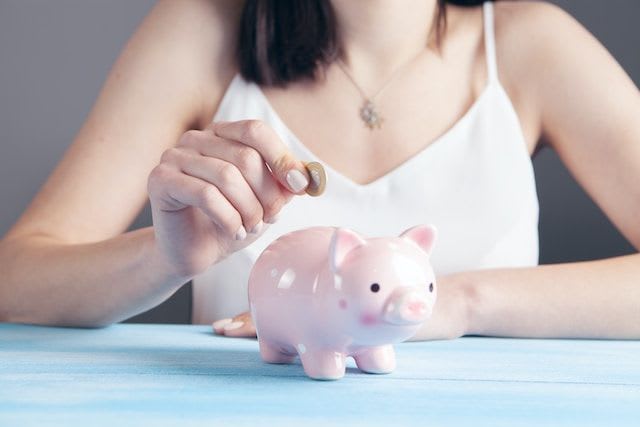 woman's hands holding piggy bank and putting it into a piggy bank