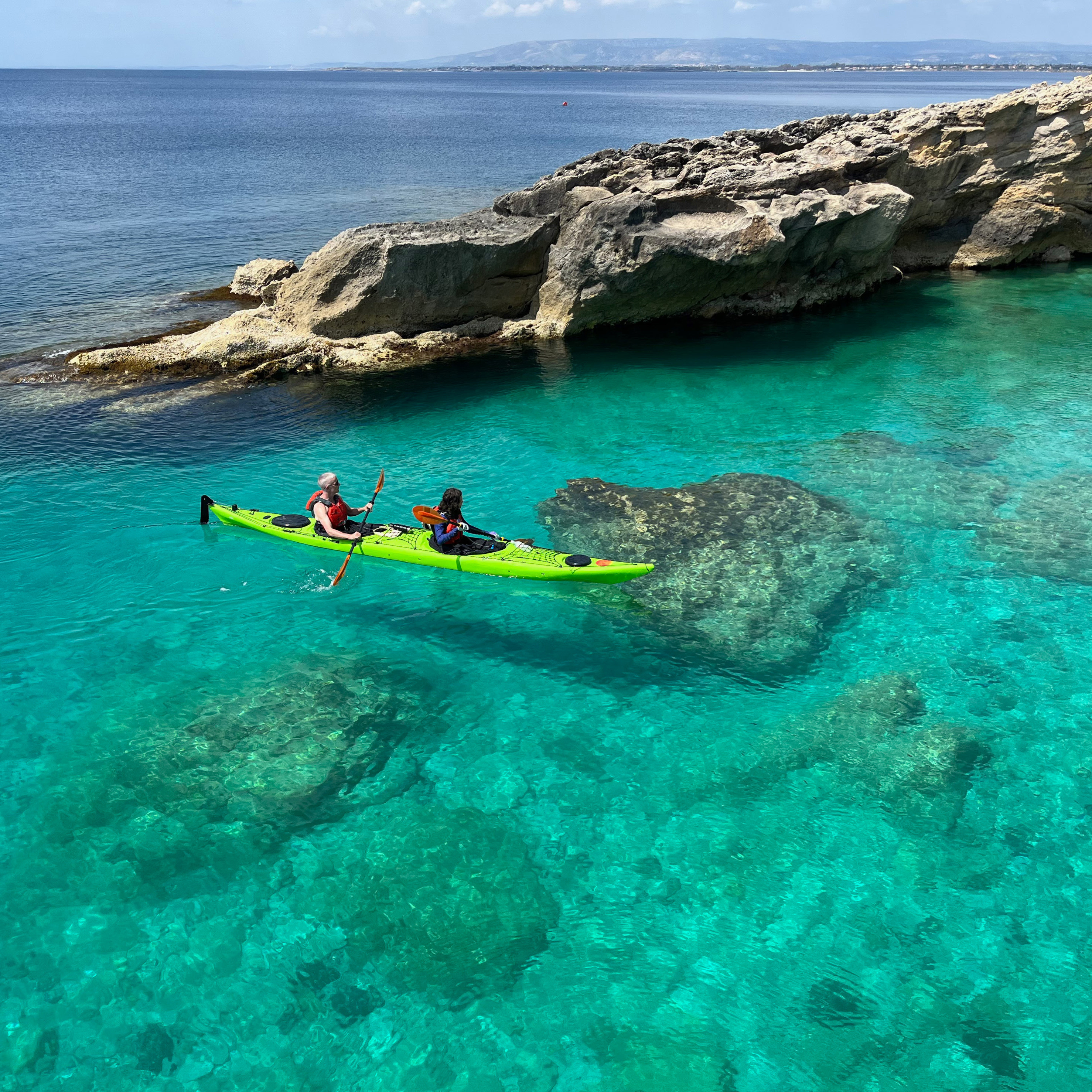 Couple paddling in clear water on Sicily kayaking tour.