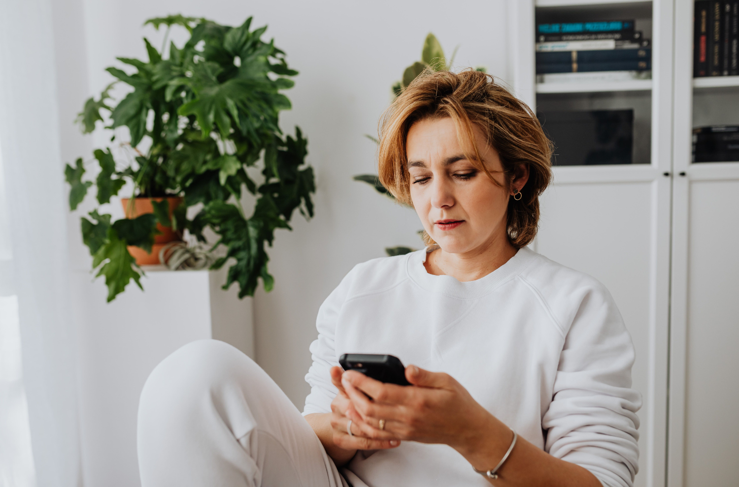 Woman sitting thoughtfully, checking her phone, still deciding whether to book a consultation